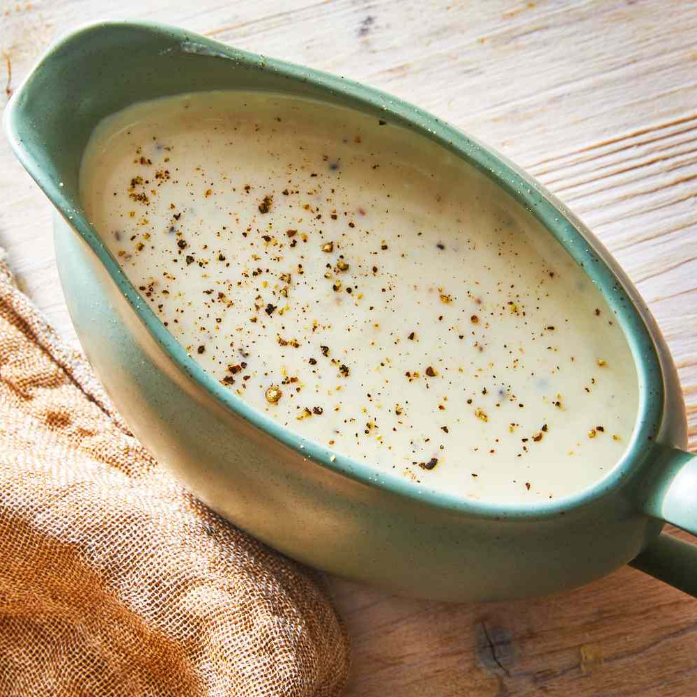 Green gravy boat filled with creamy sauce on a wooden surface