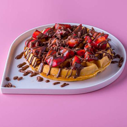 Waffle with chocolate and strawberries on a heart-shaped plate against a pink background