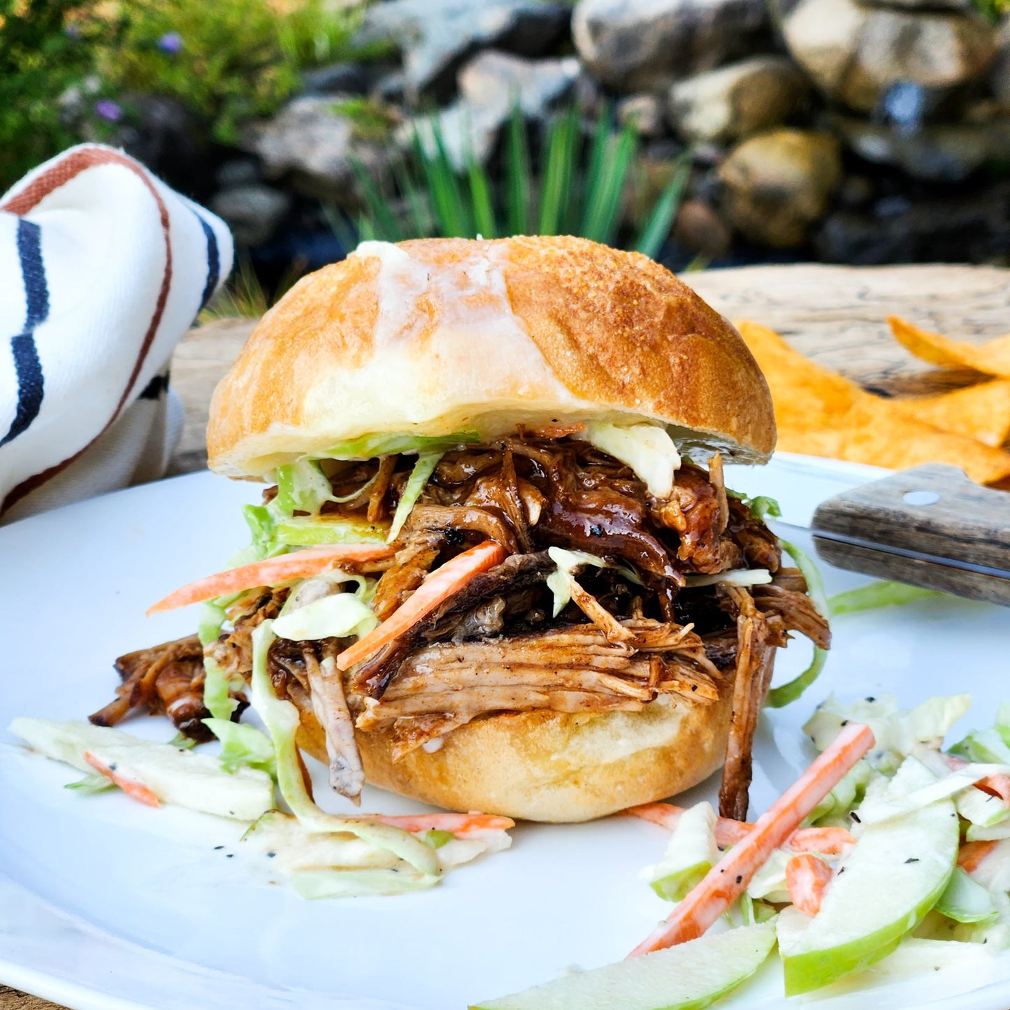 Pulled pork sandwich with coleslaw on a white plate outdoors.