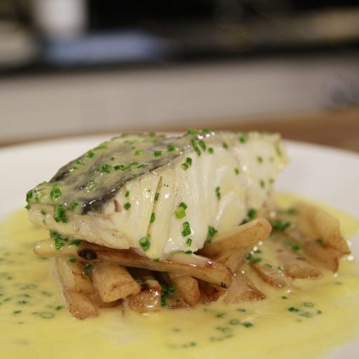 Plated dish of fish with a creamy sauce and herbs on a white plate.