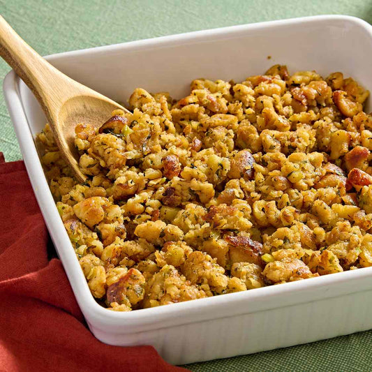 Baked stuffing in a white dish with a wooden spoon on a green tablecloth.