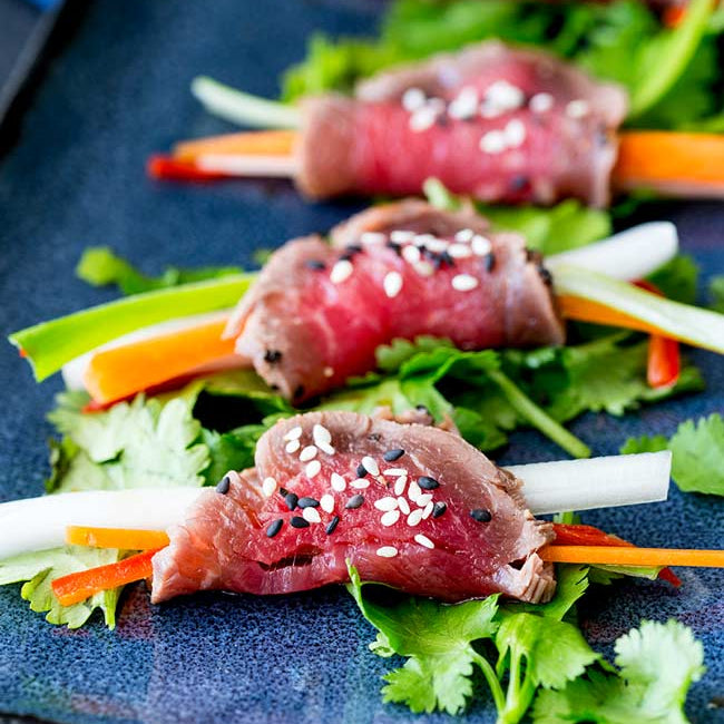 Raw beef rolls with vegetables on a blue plate