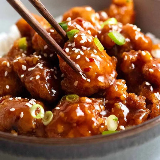 Bowl of teriyaki chicken with chopsticks, garnished with sesame seeds and green onions.