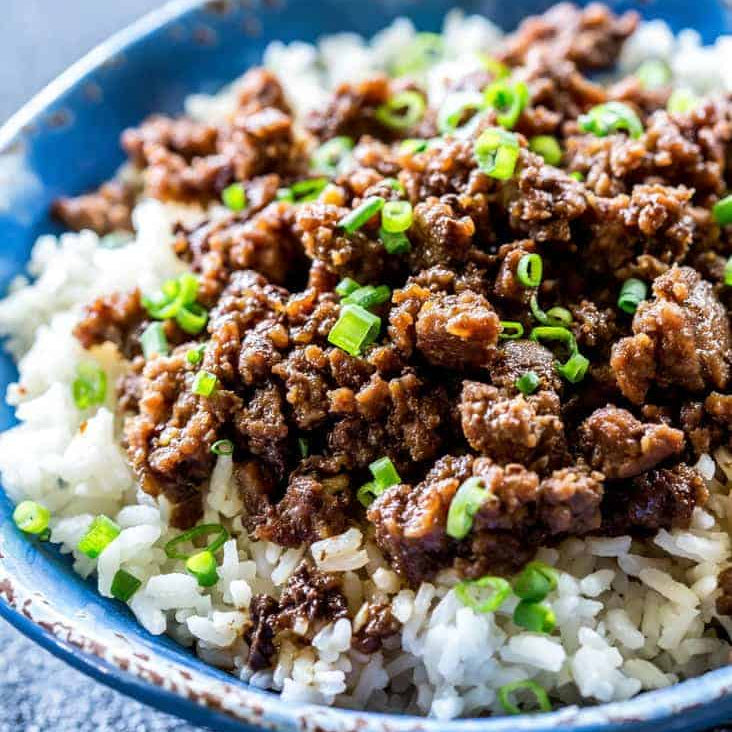 Bowl of rice topped with ground meat and green onions on a dark surface