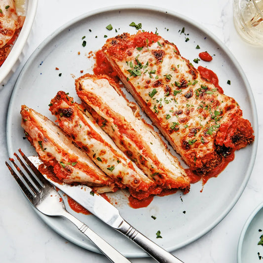Sliced chicken breast with tomato sauce on a plate with a fork and knife.