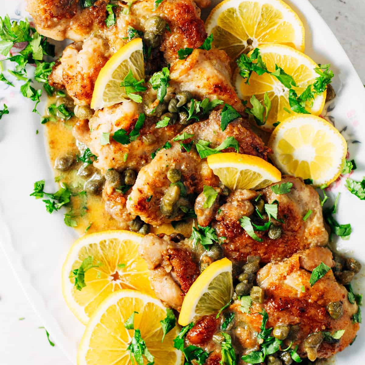 Plated dish of fried chicken with lemon slices and herbs on a white plate.