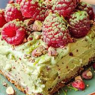 Slice of pistachio dessert with raspberries on a plate