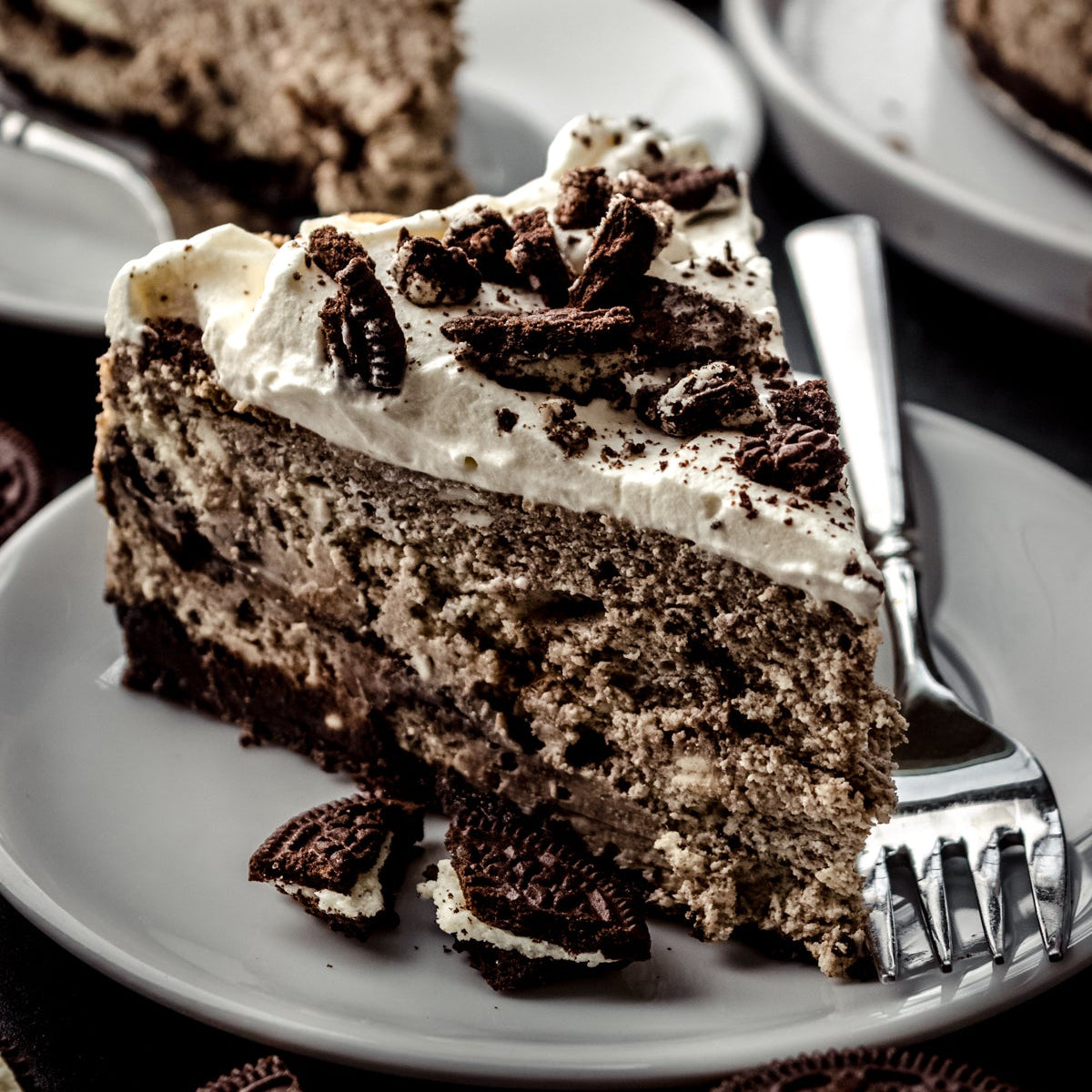 Slice of Oreo cheesecake on a plate with cookies around, close-up view.