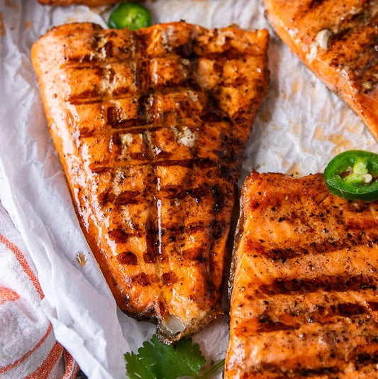 Grilled salmon fillets with jalapeños on a white paper background