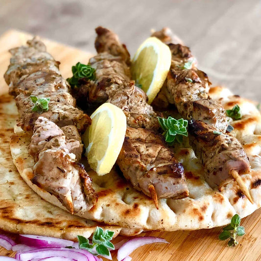 Lamb skewers with flatbread and lemon wedges on a wooden board