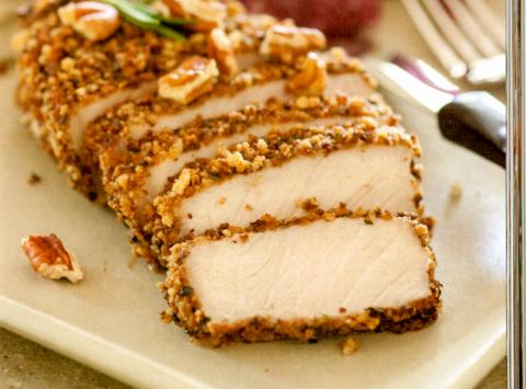 Sliced breaded chicken breast on a plate with pecans and a fork.