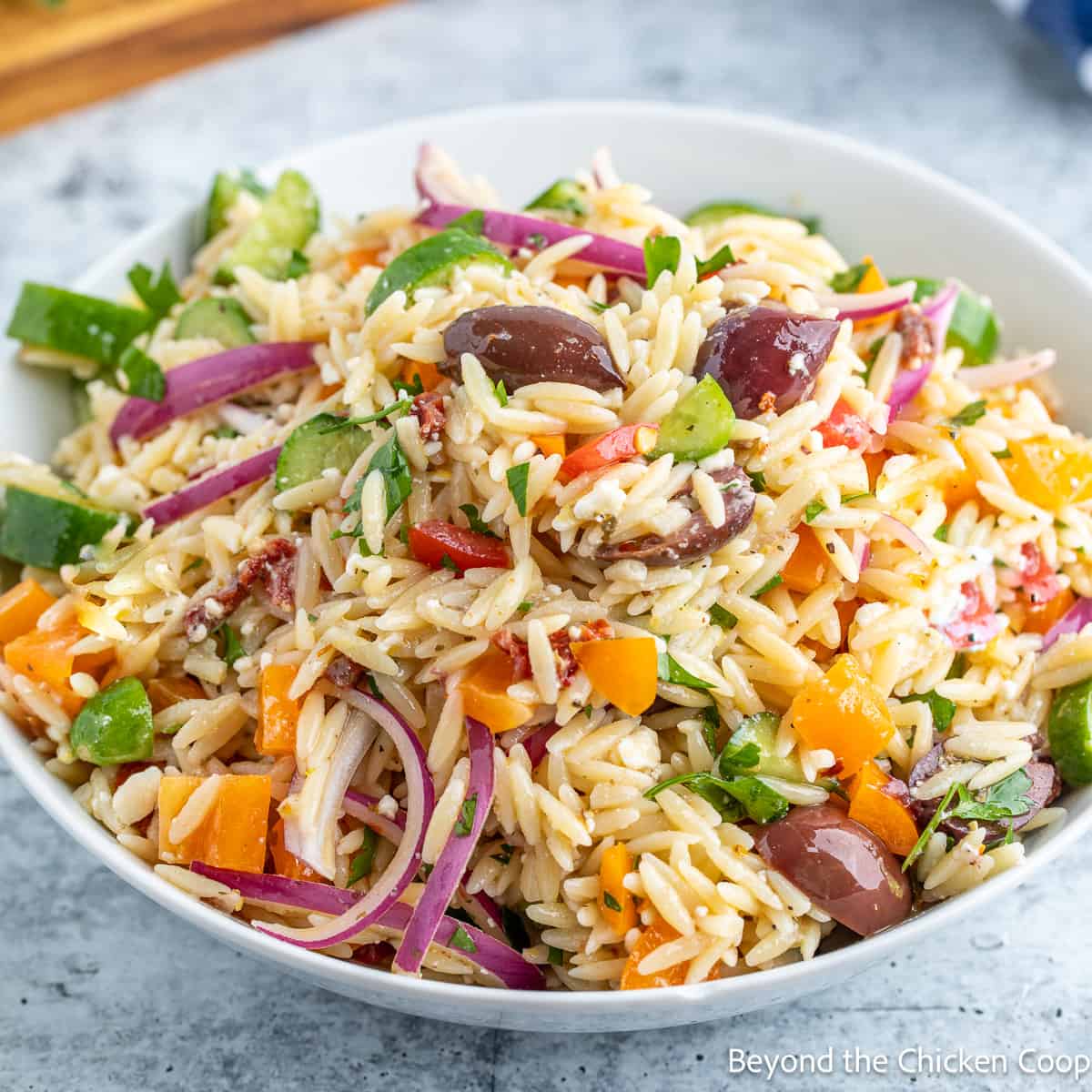 Orzo pasta salad with vegetables and olives in a white bowl on a gray surface.