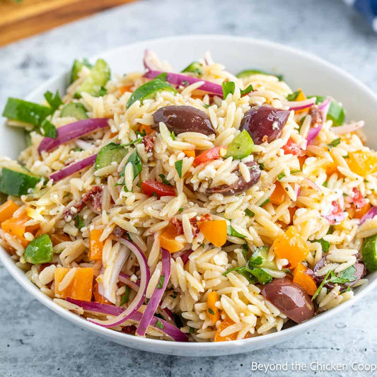 Orzo pasta salad with vegetables and olives in a white bowl on a gray surface.