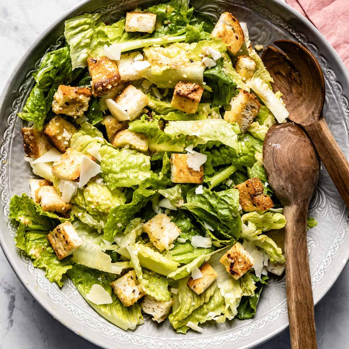 Caesar salad with croutons in a gray bowl with wooden spoons.