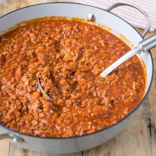 Bowl of red bolognese sauce on a wooden surface