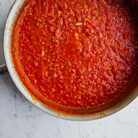 Red tomato sauce in a metal pot on a marble surface