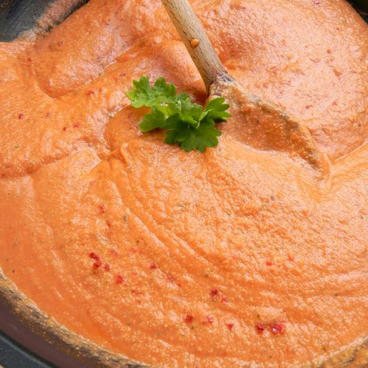 Close-up of a bowl of creamy orange soup with a garnish of green parsley.