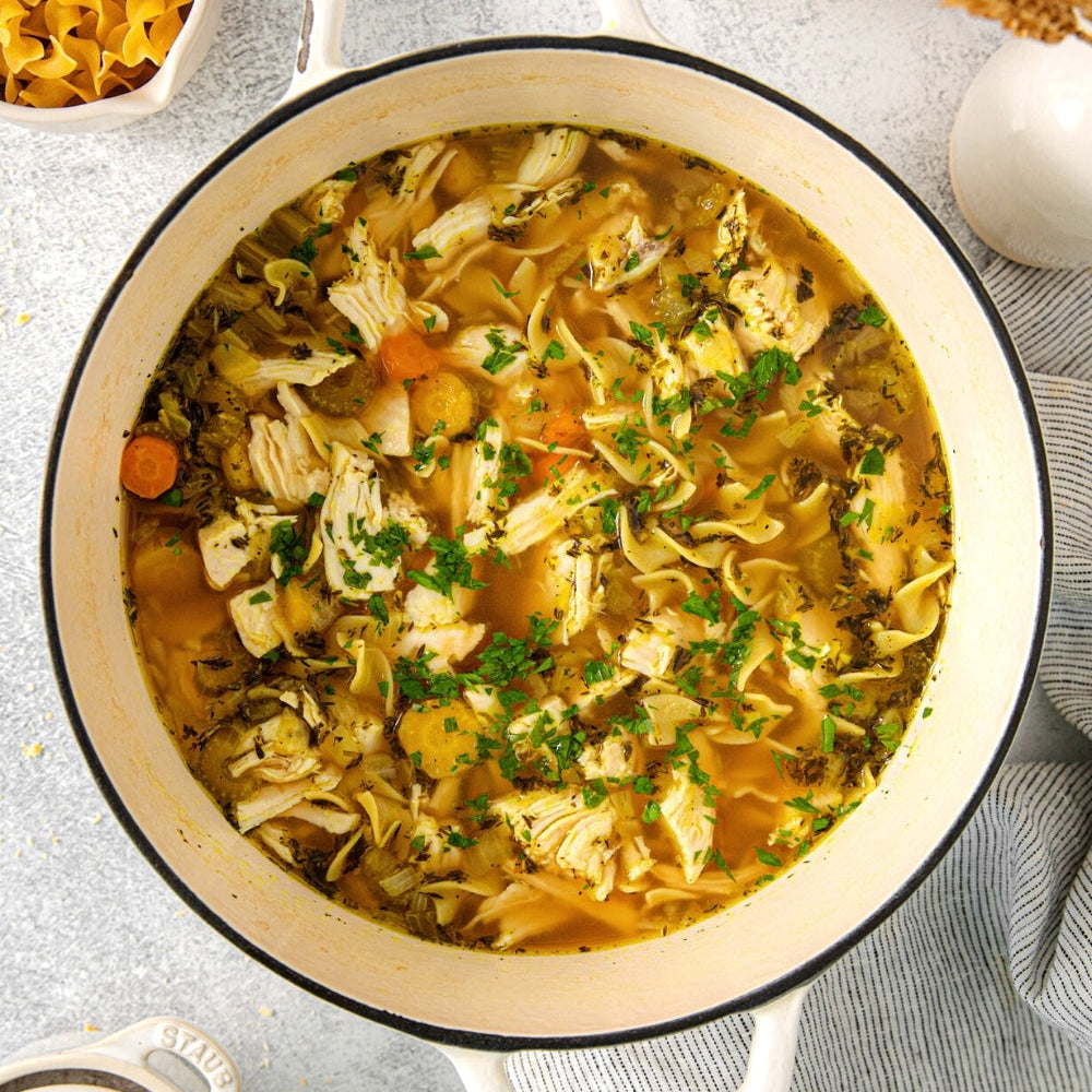 Pot of chicken noodle soup on a gray surface with ingredients around