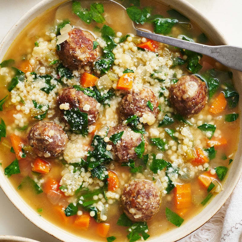 Meatball soup with vegetables in a bowl on a white table
