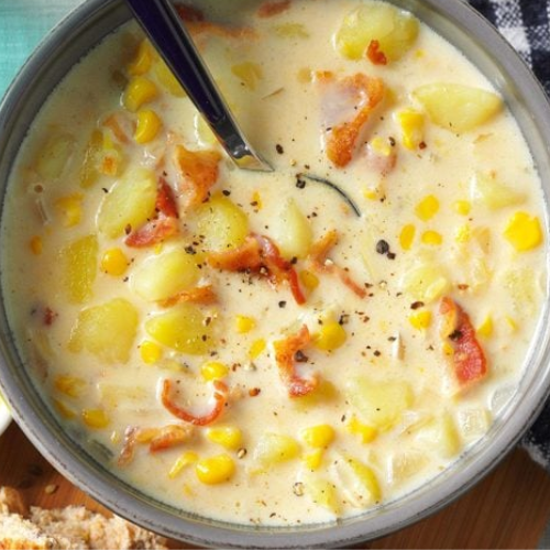 Bowl of creamy corn chowder with bacon and potatoes, served with a spoon.