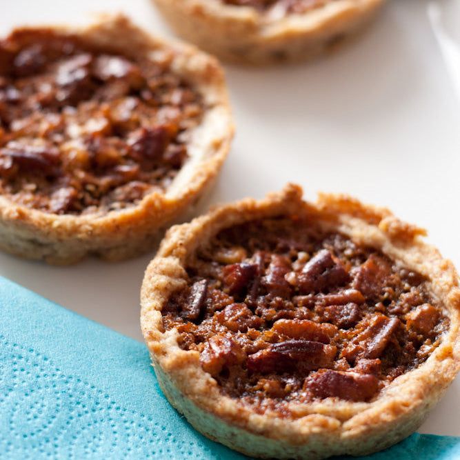 Three pecan tarts on a white plate with a blue napkin