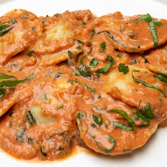 Ravioli in a rich tomato-based sauce, garnished with fresh green herbs, served on a white plate.